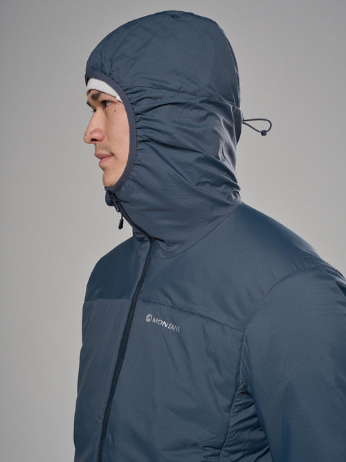 A man in profile wearing a dark slate blue hooded puffer jacket with a visible Montane logo on the chest, set against a solid gray studio background.