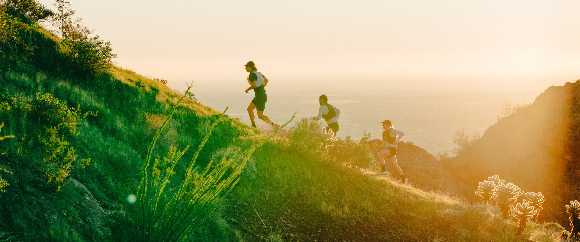 Three people running on a grassy hill at sunset